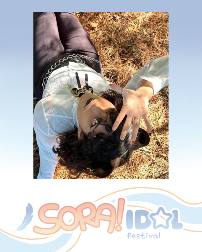 Person lying on pine needles outdoors, wearing dark pants and a white shirt, hand raised toward sunlight